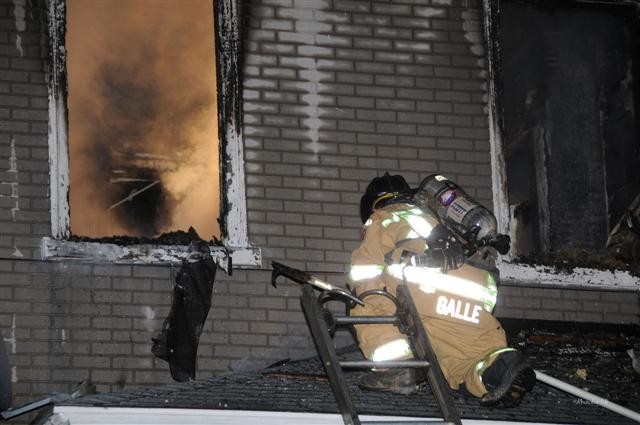 Firefighter Chris Galle operates on the porch roof at the Fourth Street house fire.